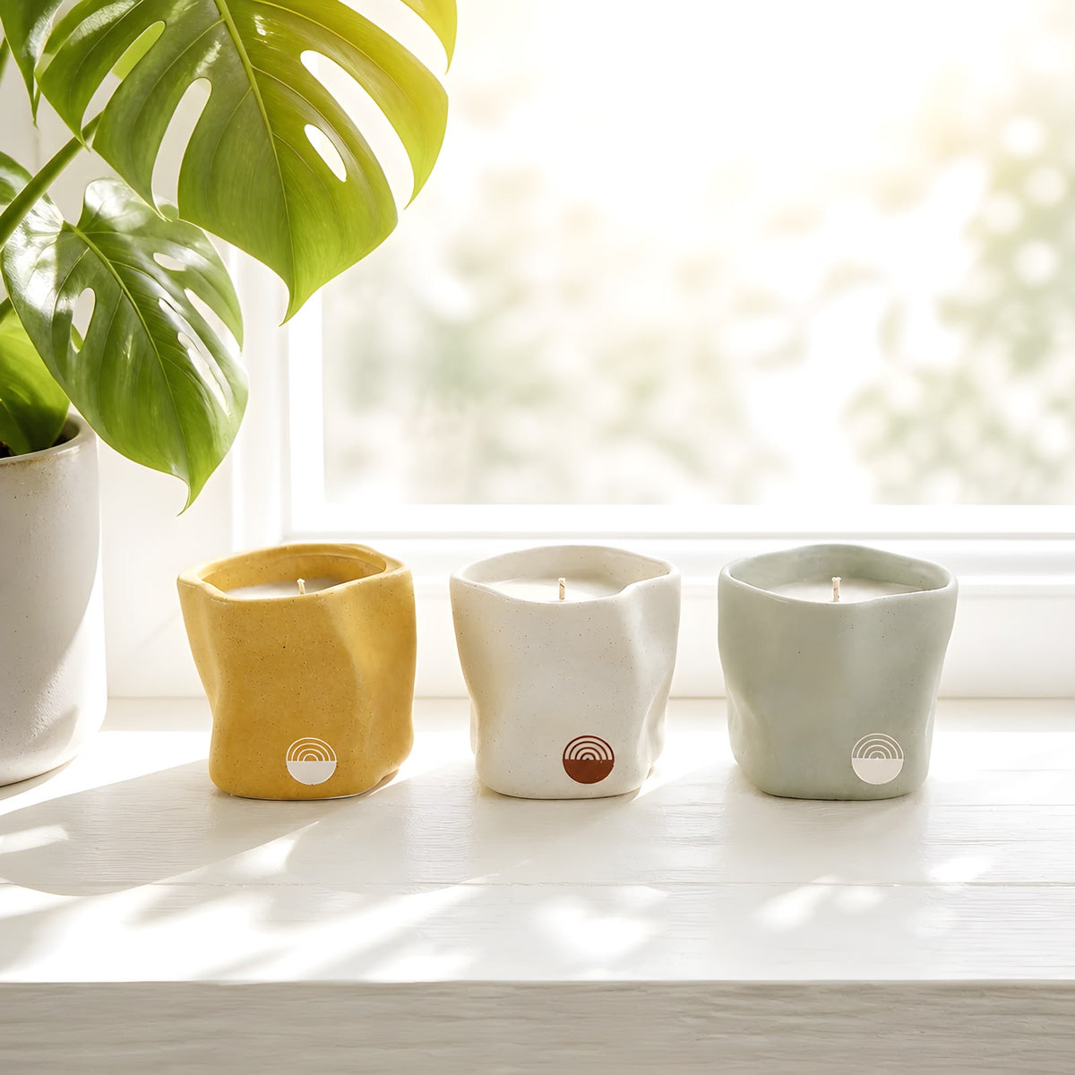 Velas artesanales KNDEL Triada en amarillo, blanco y verde junto a una ventana